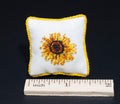 Finished  sunflower petit point pillow with yellow trim beside an inch ruler