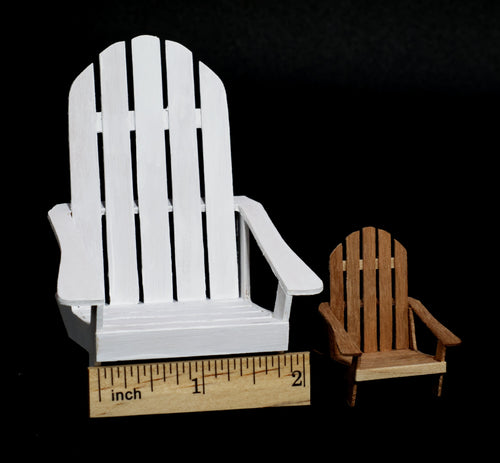 A miniature white Adirondack chair  in 1:12 scale shown next to a smaller brown wooden chair (1:24 scale) and a wooden ruler for scale, set against a solid black background.